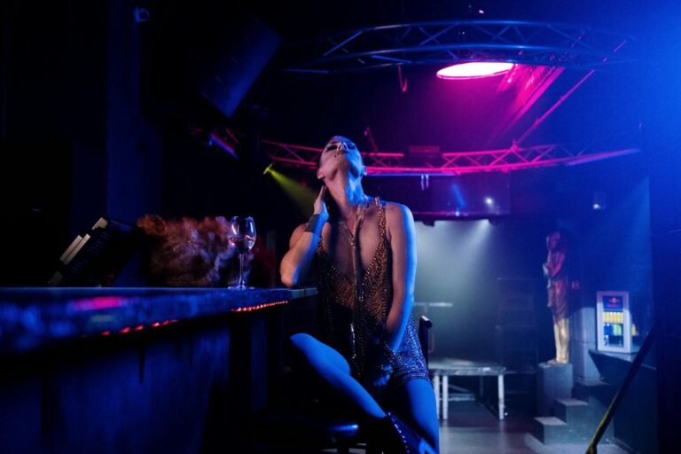 A Glamorous Performer In A Nightclub With Vibrant Lighting And Dramatic Atmosphere.