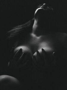 A dramatic black and white artistic nude photograph featuring a woman in a sensual pose.